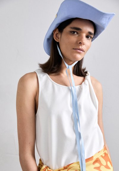 Light blue bucket hat with a wide brim, gold button detail, and blue ribbon tie. White sleeveless top and orange patterned skirt.