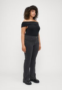 Svart bodysuit med avklippta axlar och rynkade detaljer, matchad med mörkgrå utsvängda jeans och kraftiga svarta plattformsskor med dekorationer.