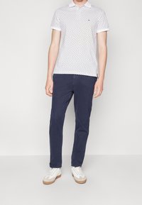 Vit polo med marinblå prickar, korta ärmar och krage, matchad med marinblå byxor och vita sneakers med beige detaljer.