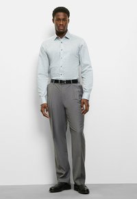 Hellblaues Hemd mit Knopfleiste und kleinem Muster, graue Anzughose und schwarze Schuhe. Das Hemd hat einen Standardkragen und lange Ärmel.