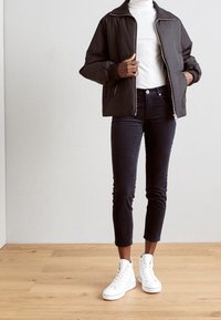 Czarna pikowana kurtka z wysokim kołnierzem, zestawiona z ciemnymi dżinsami i białymi sneakersami typu high-top. Posiada zamek błyskawiczny z przodu oraz dopasowane mankiety.