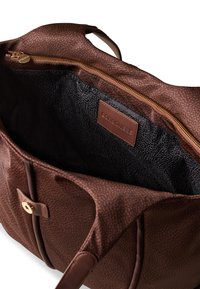 Brown patterned tote bag made of textured material, featuring a zip closure, leather accents, and a black fabric lining.
