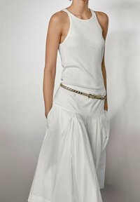 Débardeur blanc à côtes associé à une jupe blanche fluide avec des plis et des poches, rehaussée par une ceinture à clous métalliques. Design simple et épuré.