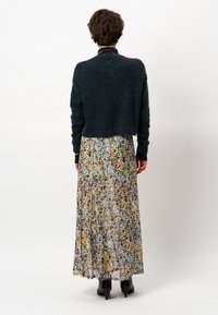 Donker, geknipt sweater gemaakt van een fuzzy materiaal, gecombineerd met een lange, bloemenrok in pasteltinten. Zwarte hakken maken de look compleet.