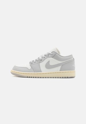Sneaker in pelle grigia chiara con dettagli bianchi, design basso, collo imbottito e suola in gomma texturizzata. Presenta l'iconico logo Swoosh.