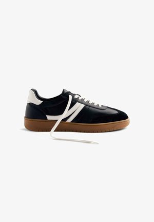 Sneaker in pelle nera con accenti bianchi, pannelli testurizzati e una suola in gomma marrone chiaro. Presenta lacci bianchi e una forma allungata.