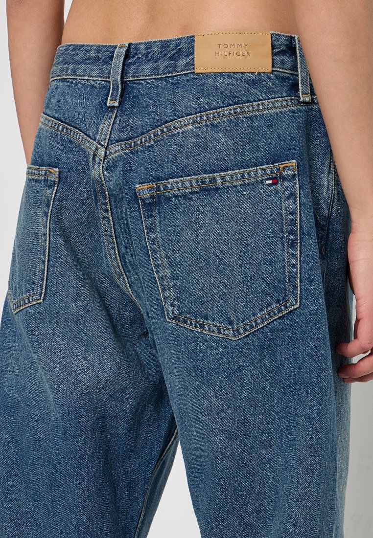 Niebieskie dżinsy o wysokim stanie, z skórzaną łatą z logo, dwoma tylnymi kieszeniami i widocznym szwem dla dodatkowej tekstury.