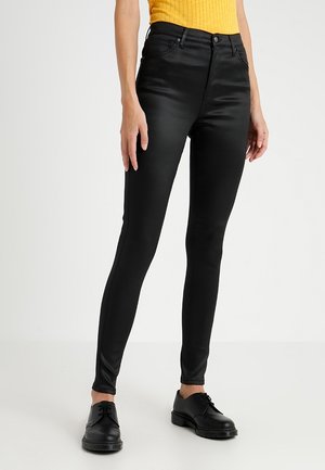 Černé, vysoké skinny kalhoty vyrobené z hladkého, elastického materiálu. Mají přední kapsy a přiléhavý střih, doplněné černými botami.