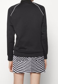 Svart sweatshirt med vita ränder vid axlarna, kombinerad med en svartvit rutig kjol. Mjukt material, ledig passform.