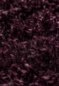 Plush, dyb lilla tekstil med en tykk, shaggy struktur. Fibrene er lange og krøllede, hvilket skaber en blød, taktil overflade.