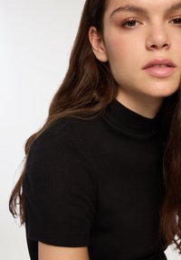 Czarny prążkowany sweter z wysokim dekoltem i krótkimi rękawami; gładka tekstura z delikatnymi liniami i detalami krawieckimi na ramieniu.