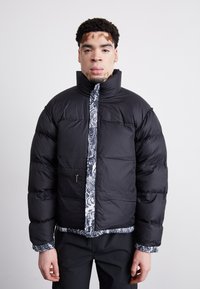 Crni puffer sako s visokim ovratnikom i uzorkovanom unutrašnjošću. Ima džep sa patentnim zatvaračem i strukturiranu podlogu. Glatki, elegantni vanjski materijal.