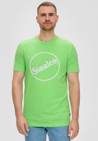 Groene katoenen t-shirt met een ronde hals en korte mouwen. Bevat een wit circulair logo met de tekst "Sinalco" in het midden.