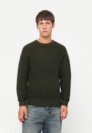 Maglione in maglia verde scuro con collo rotondo e polsini a costine. Presenta un motivo testurizzato ed è abbinato a jeans blu chiaro.