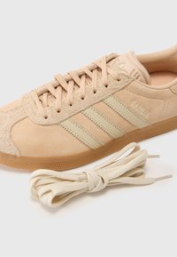 Beige suède sneaker met drie beige strepen, textuur op de neus, rubberen zool en bijpassende veters. Geperst logo op de tong.