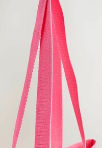 Bright pink textured fabric straps hanging against a plain light background, showing detailed woven pattern.