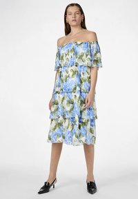 Φόρεμα με γυμνούς ώμους και διπλές στρώσεις με μπλε λουλουδάτο σχέδιο σε λευκό φόντο. Κατασκευασμένο από ελαφρύ ύφασμα, με βολάν και άνετη γραμμή.