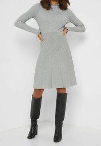 Haut côtelé gris à manches longues avec des accents en perles, associé à une jupe plissée grise et des bottes noires à talons montant jusqu'aux genoux. Texture lisse, design ajusté.