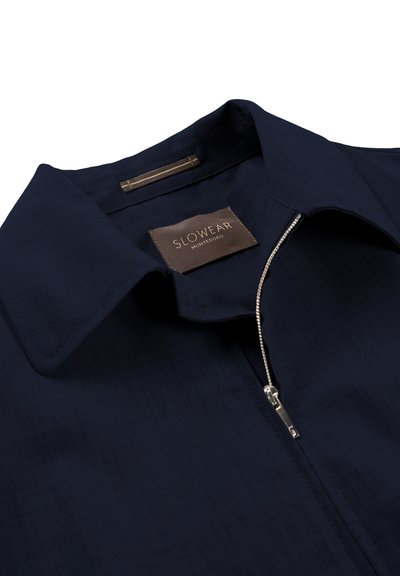 Navy blue zip-up shirt with a collar, featuring a textured fabric, a silver zipper, and a branded tag reading "SLOWEAR MONTEDORO."