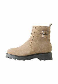 Semišové kotníkové boty světle hnědé barvy se dvěma ozdobnými sponami. Mají masivní černou gumovou podrážku a zaoblený design špičky.