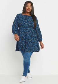 Sininen kukkakuosiset mekko, jossa on pitkät hihat, koota oleva vyötärö ja hulppea alaosa. Yhdistetty kapeisiin farkkuihin ja valkoisiin tennareihin.