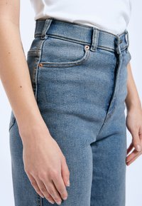 Jeans de tiro alto en tejido de denim, con una textura suave, remaches de cobre y un diseño clásico de cinco bolsillos.