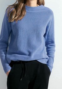 Sininen neulottu pusero, jossa pyöreä pääntie, pitkät hihat, pehmeä tuntuma ja rento istuvuus, yhdistetty mustiin housuihin, joissa on sivutaskut.