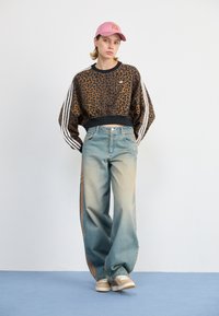 Leopardenmuster-Cropped-Sweatshirt mit schwarzem Saum, kombiniert mit hellblauen weitem Jeans, die orangefarbene Seitenstreifen und braune Sneakers haben.