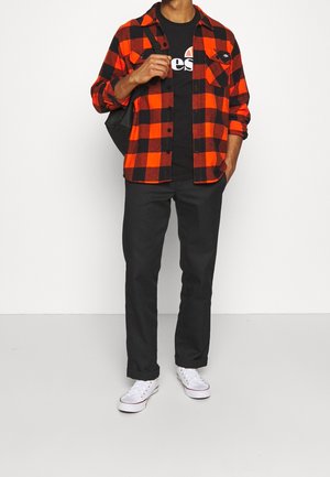 Camicia di flanella a quadri rossi e neri, t-shirt nera con stampa, pantaloni neri e sneakers bianche. Colori uniformi e pattern distinti visibili.