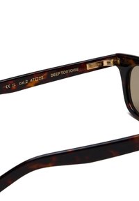 Occhiali da sole in tartaruga con lenti a gradiente marroni, dettagli dorati sulle tempie, montatura strutturata e incisioni all'interno.