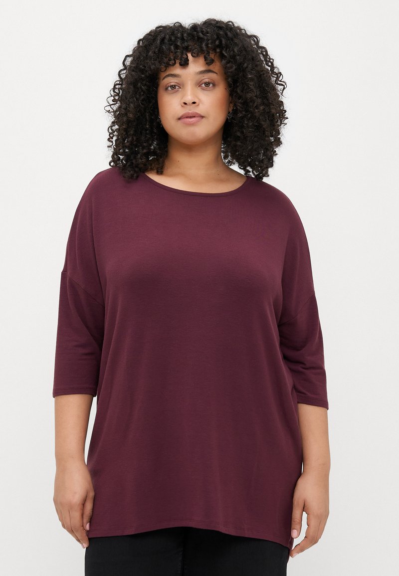 Camisola larga bordeaux com decote redondo e mangas três quartos, feita de um tecido suave. Bainha ligeiramente curva para um ajuste descontraído.