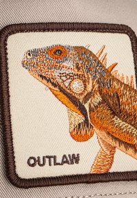 Embroidery patch of a detailed orange and brown iguana head with the word "OUTLAW" stitched below on beige fabric.