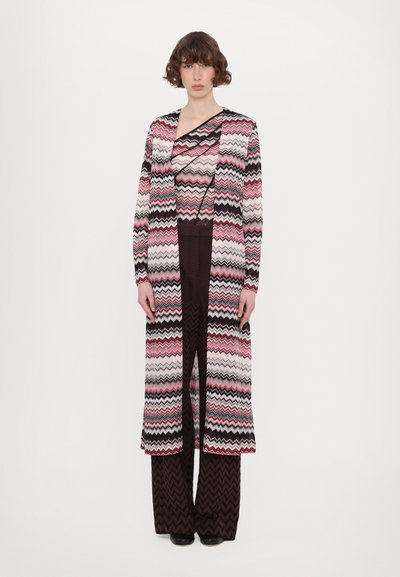 Cardigan cu model zigzag multicolor, purtat peste un top asortat și pantaloni largi maro. Cardiganul are mâneci lungi și o fanta frontală.