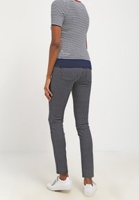 Marinblå och vit randig topp med en röd halsringning, matchad med tajta mönstrade byxor med en liten vit geometrisk design. Vita sneakers.