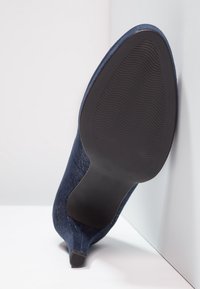Zapato de tacón alto de ante azul marino con punta afilada, tejido texturizado y suela de goma negra lisa con patrones de olas.