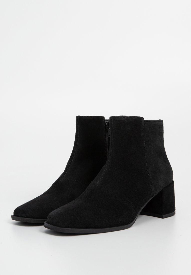 Ein Paar schwarze Wildleder-Ankle Boots mit Blockabsätzen und seitlichen Reißverschlüssen auf einem schlichten weißen Hintergrund.
