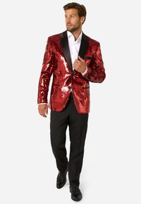 Sarkans mirdzošs žakets ar melniem satīna uzgaļiem, saskaņots ar melnām biksēm un apaviem. Gluda tekstūra ar atspīdošiem mirdzošiem akmentiņiem, kas piešķir papildu spīdumu.