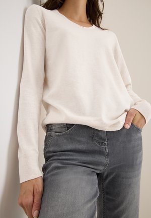 Pull long à manches longues rose pâle avec un col rond, associé à un jean en denim gris à coupe classique avec poches avant.