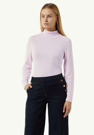 Helles rosa Rollkragenpullover aus weichem Strickmaterial, mit langen Ärmeln und subtilen Schulterdetails. Kombiniert mit dunklen, weiten Hosen.