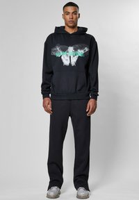 Felpa nera con una stampa grafica di una farfalla e testo, abbinata a pantaloni neri coordinati. Il materiale sembra morbido e casual. Scarpe argento.