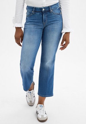 Hellblaue Jeans mit geradem Bein, mittelhoher Taille und subtiler Ausbleichung. Kombiniert mit weißen und grauen Sneakern. Minimalistische Details.