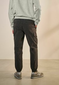 Dunkelgraue Cargo-Hosen aus strapazierfähigem Stoff; mit elastischen Bündchen und Seitentaschen; kombiniert mit grauen Turnschuhen und einem hellgrauen Sweatshirt.
