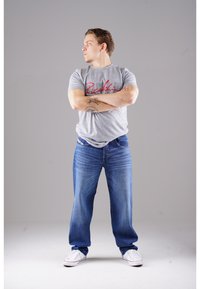 Graues T-Shirt mit rotem Logo, blaue Jeans im Denim-Stil und weiße Sneakers. Die Jeans haben eine gerade Passform und eine verblasste Waschung.