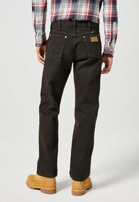 Jeans en denim noir avec des coutures claires, poches arrière renforcées présentant un motif en zigzag, et une étiquette en simili cuir sur la taille.