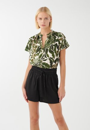 Blusa verde e crema con motivo a foglie, maniche corte e arricciate, abbinata a pantaloni corti neri con vita elastica e dettaglio annodato.