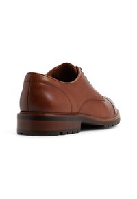 Zapato de cuero marrón con punta redonda, textura suave y costuras elevadas. Cuenta con una suela de goma marrón resistente con tracción.