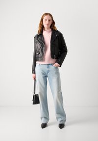 Black leather cropped jacket over a pink knitted sweater, light blue wide-leg jeans, black pointed-toe shoes, and a small black handbag.