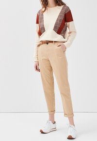 Sweatshirt crème avec des accents rouges et en plaid, associé à un chino beige et des baskets blanches avec des semelles marron. La ceinture est en matériau tissé marron.