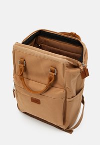 Sac à dos en tissu marron avec poignées en cuir, poche avant, poches latérales et compartiment principal partiellement ouvert laissant voir la doublure intérieure.