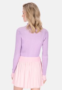 Orgonalila bordázott pulóver hosszú ujjakkal, világos rózsaszín pliszírozott miniszoknyával párosítva. A pulóveren kontrasztos bordázott derékrész található.